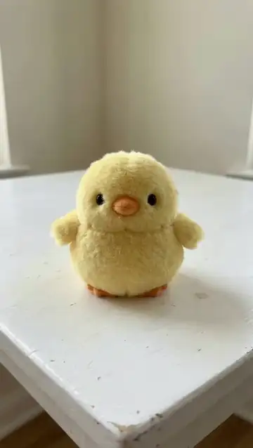 Two hands squash the plush chick flat and it puffs back up